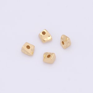 Peut inclure: Quatre perles en métal de couleur dorée avec un trou au centre. Les perles sont de forme irrégulière et ont une surface légèrement texturée.