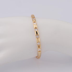 Könnte beinhalten: Ein goldenes Armreif-Armband mit klaren runden Steinen, die in einer Reihe um das Band gesetzt sind.