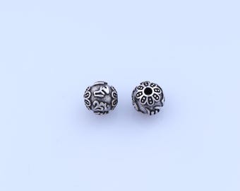 Puede incluir: Dos cuentas esféricas plateadas con intrincados patrones en relieve. Una cuenta presenta un diseño floral, mientras que la otra tiene un patrón más abstracto. Las cuentas son probablemente para la fabricación de joyas o manualidades.