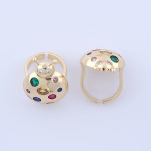 Peut inclure: Deux bagues dorées en forme de coccinelle. Chaque bague présente un motif de coccinelle avec des accents de pierres précieuses colorées. Une bague a une forme de coccinelle fermée, l'autre est ouverte. Les bagues sont sur fond blanc.
