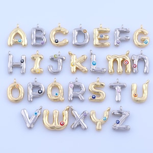 Peut inclure: Une collection de breloques de lettres de l'alphabet en or et argent. Chaque breloque présente un design unique et comprend un petit détail coloré en forme d'œil. Les lettres sont disposées en grille, présentant l'alphabet complet.