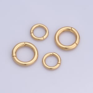 Puede incluir: Cuatro anillos de salto de metal de color dorado de diferentes tamaños. Los anillos están abiertos y tienen un acabado liso.