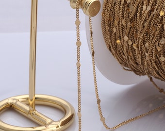 May include: A gold chain with small round discs, displayed on a gold stand. The chain is wound around a spool.
