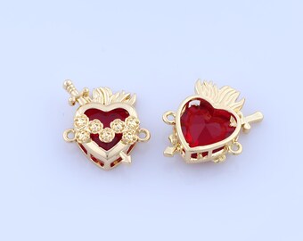 May include: Two gold-colored heart-shaped charms with red gemstone centers. Each charm features a sword, floral accents, and a flame design. The charms have small loops for attaching to jewelry.
