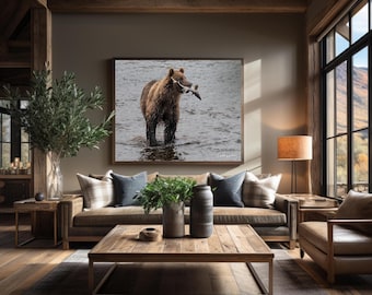 May include: A large rectangular wall art print featuring a brown grizzly bear standing in shallow water with a fish in its mouth. The photograph is displayed in a dark wooden frame and mounted on a neutral-toned wall above a brown sofa.