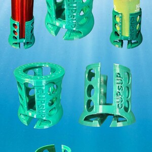 May include: Five green 3D printed plastic bottle and can holders with the word "cupsup" printed on them. The holders are designed to hold a variety of sizes of bottles and cans.