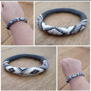 Op de afbeelding: Een zwart-witte kralen armband met een geometrisch patroon. De armband is gemaakt van kleine kralen en is flexibel.