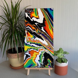 May include: Abstract painting on canvas with a colorful, swirling design in shades of black, white, green, yellow, orange, and blue. The painting is displayed on a wooden easel.