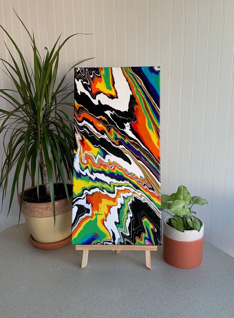 May include: Abstract painting on canvas with a colorful, swirling design in shades of black, white, green, yellow, orange, and blue. The painting is displayed on a wooden easel.