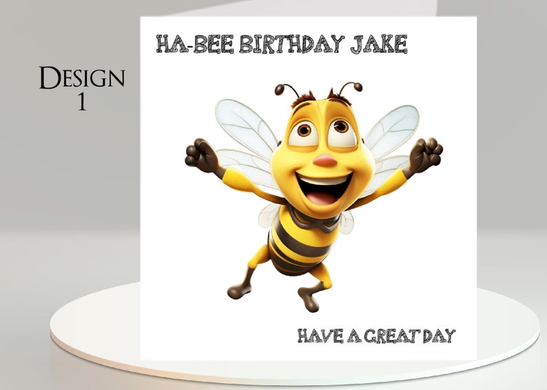 Pu&ograve; includere: Biglietto di compleanno con un'illustrazione di un'ape dei cartoni animati. L'ape gialla e nera ha le braccia tese e un grande sorriso. Il testo dice "HA-BEE BIRTHDAY JAKE" in alto e "HAVE A GREAT DAY" in basso. Il biglietto &egrave; su una superficie bianca.