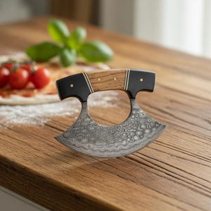 May include: A pizza cutter with a curved, patterned blade and a wooden handle with black accents. The blade has a unique, swirling design. The handle is made of light-colored wood with brass rivets. The cutter is on a wooden surface.