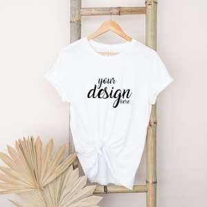 May include: White t-shirt with the text "your design here" printed on the front. The shirt is hanging on a wooden ladder.