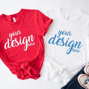 K&ouml;nnte beinhalten: Zwei leere T-Shirts, eines rot und eines wei&szlig;, mit dem Text "your design here" auf jedem. Das rote Shirt ist unten verknotet. Das wei&szlig;e Shirt ist unten verknotet und liegt auf einer blauen Jeans und einem Paar wei&szlig;en Sneakers.