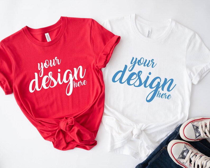 K&ouml;nnte beinhalten: Zwei leere T-Shirts, eines rot und eines wei&szlig;, mit dem Text "your design here" auf jedem. Das rote Shirt ist unten verknotet. Das wei&szlig;e Shirt ist unten verknotet und liegt auf einer blauen Jeans und einem Paar wei&szlig;en Sneakers.