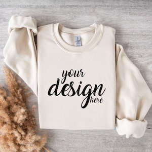 May include: A cream coloured sweatshirt with the text "your design here" in black lettering.