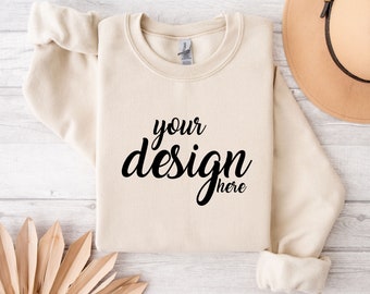 May include: A beige sweatshirt with the text "your design here" printed on the front. The sweatshirt is laid flat on a white wooden surface.