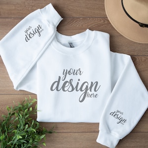 Op de afbeelding: Witte trui met lange mouwen en een ronde hals. De trui heeft de tekst "your design here" gedrukt op de voorkant en beide mouwen.
