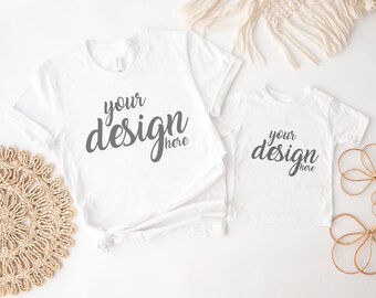 May include: Two white t-shirts with the text "your design here" in gray on them. The shirts are laid out on a white surface.
