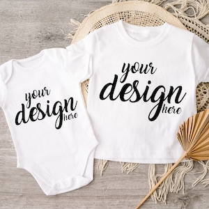 May include: Two white baby onesies with short sleeves. The onesies have the text "your design here" printed in black on the front.