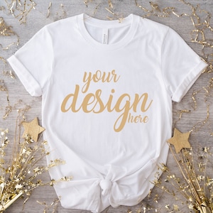 May include: White t-shirt with the text "your design here" in gold lettering on a wood background with gold confetti.