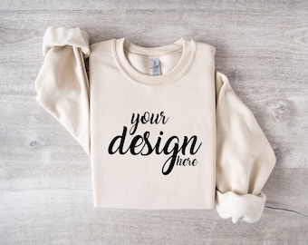 May include: A cream colored sweatshirt with the text "your design here" printed in black on the front.