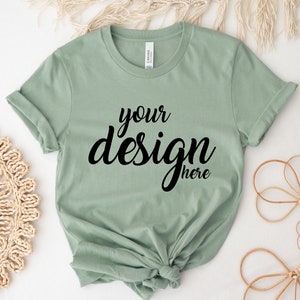 May include: A sage green t-shirt with the text "your design here" printed in black.