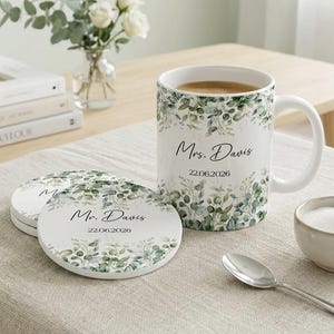 May include: A white ceramic mug and matching coasters with a green and white botanical design. The mug is filled with coffee and features the text "Mrs. Davis 22.06.2026". The coasters also have the text "Mr. Davis 22.06.2026".