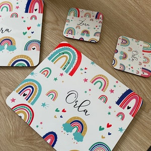 May include: Set of three rainbow-themed coasters with white backgrounds and colorful rainbows, stars, and hearts. The coasters are personalized with the names "Orla", "Zara", and "Olly".