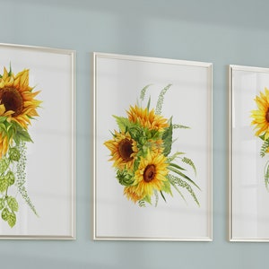 May include: Three framed watercolor paintings of sunflowers with green leaves and stems. The sunflowers are yellow with brown centers. The paintings are on a light blue wall.