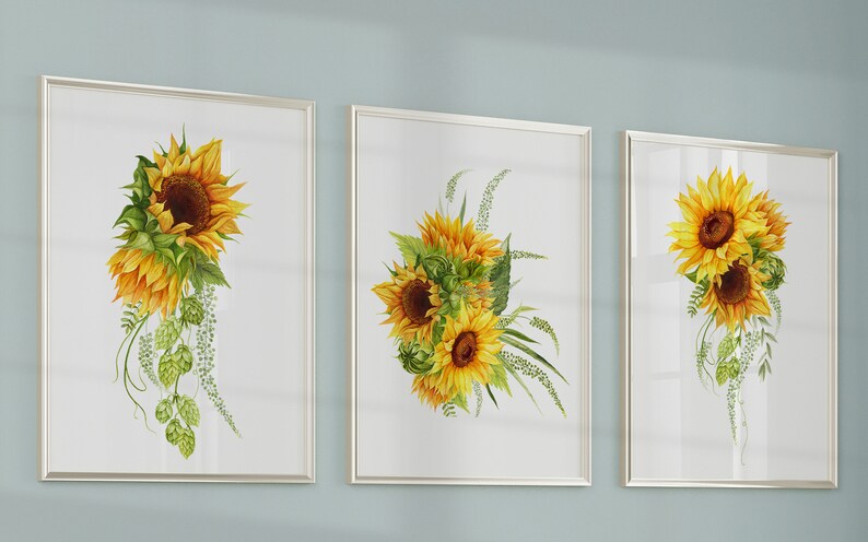 May include: Three framed watercolor paintings of sunflowers with green leaves and stems. The sunflowers are yellow with brown centers. The paintings are on a light blue wall.