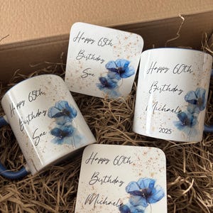 May include: Four personalized birthday gifts: two mugs and two coasters. The mugs and coasters are white with blue floral designs and the text "Happy 65th Birthday Sue" and "Happy 60th Birthday Michael 2025". The gifts are in a brown box.
