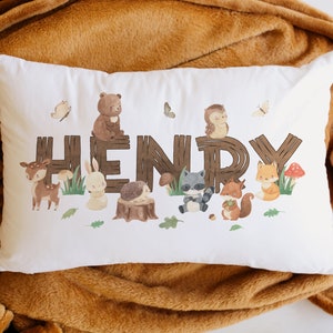 May include: White pillow with the name "HENRY" spelled out in brown wooden letters. Each letter is decorated with a different woodland animal, including a bear, owl, deer, rabbit, raccoon, squirrel, and fox.