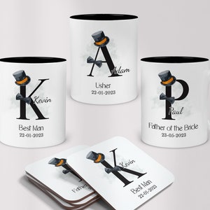 May include: Three black and white mugs with a black handle and a white interior. Each mug features a black letter with a black top hat and bow tie on top. The letters are A, K, and P. The mugs are personalized with names and titles, such as "Usher", "Best Man", and "Father of the Bride". The mugs are accompanied by a set of four coasters with the same design as the mugs.