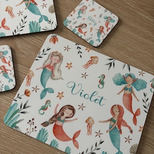 May include: Set of four white coasters with a mermaid theme. The coasters feature a watercolor design of mermaids, seahorses, and starfish. The coasters are personalized with the names "Betty" and "Violet".