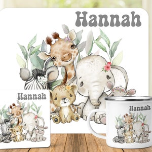 May include: A white rectangular placemat, a square coaster, and a white enamel mug, each featuring a watercolor illustration of a baby giraffe, elephant, zebra, lion, and rhino with green leaves and the name Hannah printed in grey text.