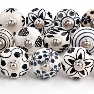 May include: A set of 15 black and white ceramic drawer knobs with various patterns. The knobs are round and have a silver metal base.