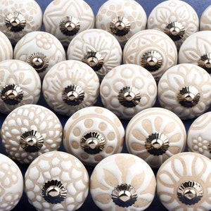 collection of white ceramic drawer knobs with intricate floral patterns and silver accents. The knobs are arranged in a basket lined with peach-colored fabric.