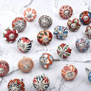 May include: A collection of 20 ceramic cabinet knobs with colorful floral patterns. The knobs are round and have a silver metal base.