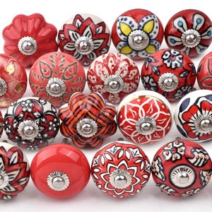 Red ceramic knobs with hand-painted white floral and mandala designs; assorted cabinet knobs for furniture and home décor.