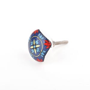 Può includere: Un pomello decorativo per mobili con un design floreale bianco, blu, rosso e giallo. Il pomello ha una faccia rotonda e piatta con una vite metallica per il fissaggio. Il design presenta un motivo centrale di fiori e foglie.
