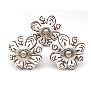 May include: Three white ceramic cabinet knobs with a brown floral design. Each knob has a silver metal base.