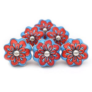 Może przedstawiać: Sześć niebieskich ceramicznych gałek do szafek z czerwonymi wzorami kwiatów. Każda gałka ma srebrny środek.