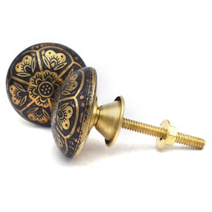 Etched brass flower cabinet knob with ornate gold pattern on dark background; decorative cabinet knobs for dresser hardware.