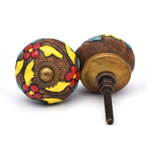 May include: Two brown ceramic cabinet knobs with a floral design. The knobs have yellow, red, and blue flowers on a brown background. The knobs have a brass screw.