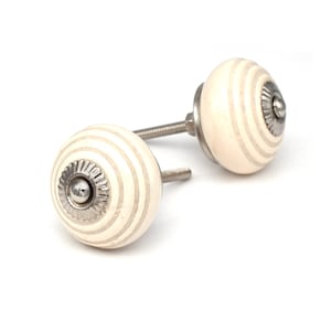 Peut inclure: Deux boutons de cabinet en céramique blanche avec des accents en métal argenté et un motif rayé.