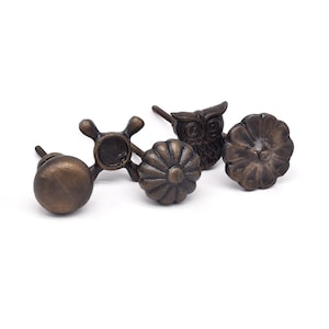 May include: Set of four antique bronze cabinet knobs with different designs: a flower, an owl, a wheel, and a round knob.