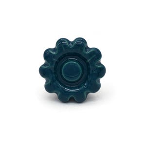 May include: Teal blue ceramic cabinet knob with a flower-shaped design. The knob has a raised center circle.