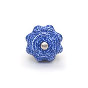 Op de afbeelding: Een blauw-witte keramische kastknop met een bloemenontwerp. De knop heeft een zilveren metalen midden en een geschulpte rand. De decoratieve hardware staat tegen een witte achtergrond.