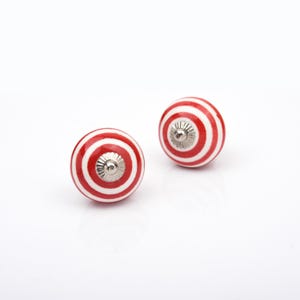 May include: Two round ceramic cabinet knobs featuring a vibrant red and white concentric circle pattern. Each knob is finished with a polished silver-tone metal center piece that includes a small, raised circular detail at the very top.