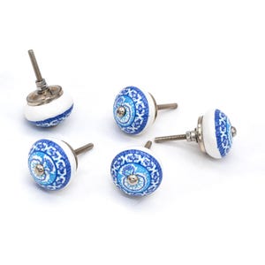 May include: A collection of five ceramic cabinet knobs. The knobs are white with a blue and turquoise floral pattern. Each knob has a metal screw for installation. The knobs are round and have a decorative design.